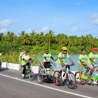Riders in lime shirts on a lagoon-side road with palms