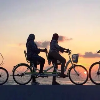 Silhouetted riders, including a tandem, at sunset over the sea