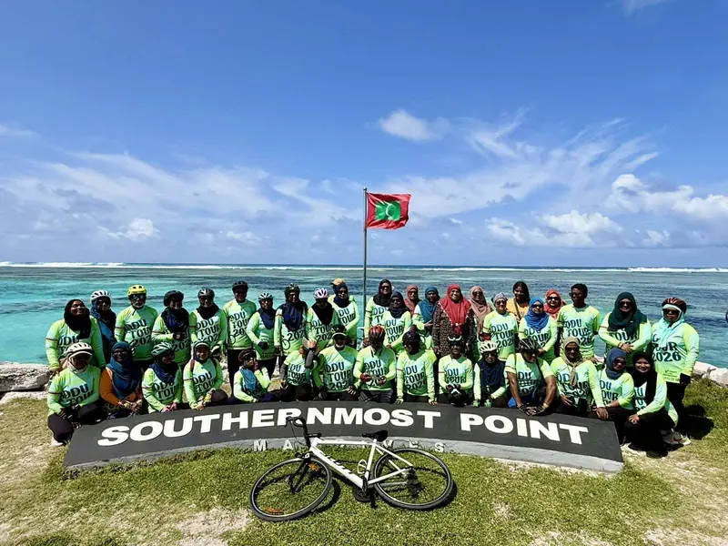 Bike Maldives riders with flag and sea at the Southernmost Point, Addu