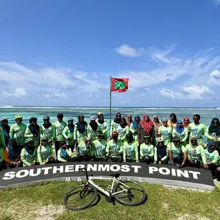 Bike Maldives riders with flag and sea at the Southernmost Point, Addu