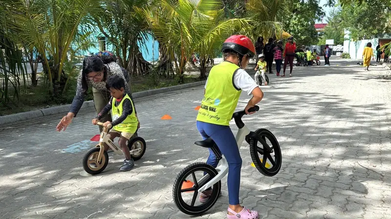 Two young children on balance bikes with coaches nearby
