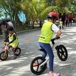 Two young children on balance bikes with coaches nearby