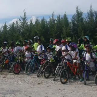 Line of young riders and adult leaders with bikes on a white sand track